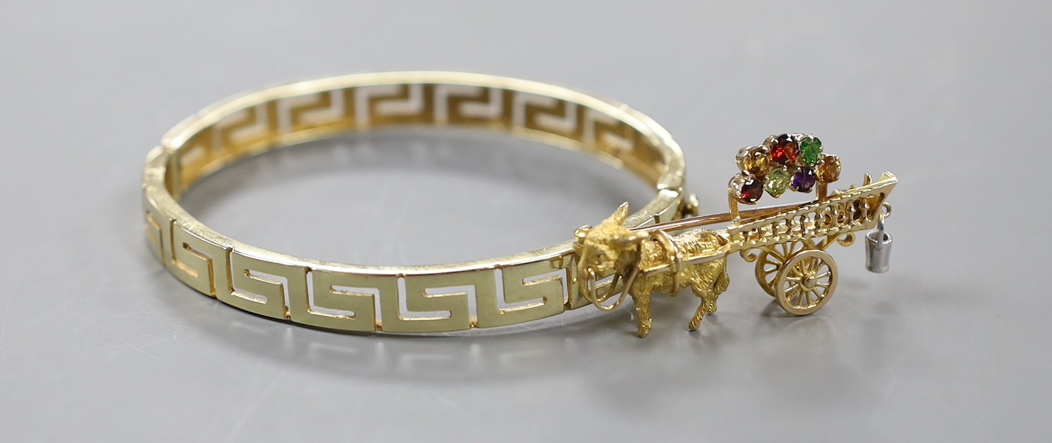 A modern yellow metal hinged bangle with Greek Key decoration and a 9ct donkey and cart charm, gross weight 23.2 grams.